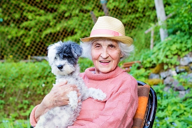 Senior woman outside in a chair holding a dog and smiling