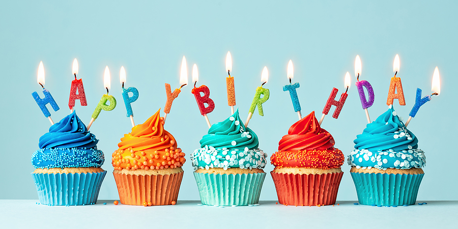 Five colorful frosted cupcakes with lit candles that say, "Happy Birthday"