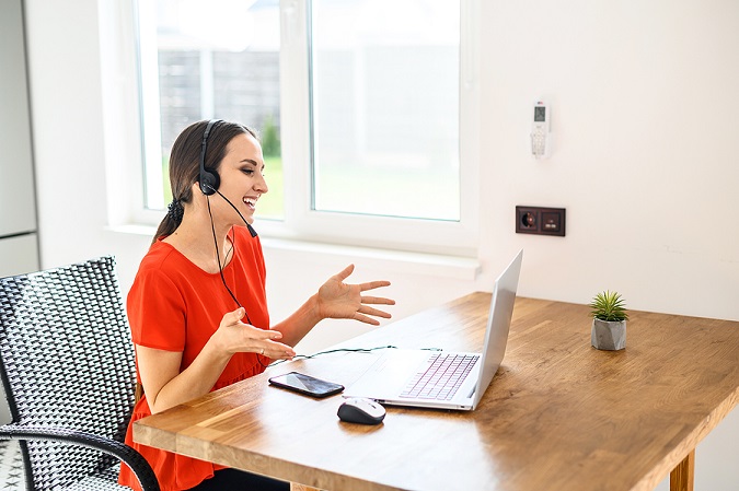 Young smiling woman woman using a headset and a laptop to converse with a remote client